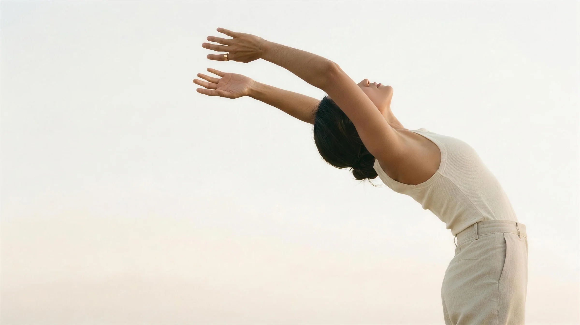 A woman in a standing backbend, arms sweeping overhead, wearing the gold Vexo ring